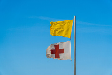 The red cross flag flying next to a yellow flag, surveillance post and sea state information