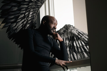 Contemplative man with black feathered wings by window