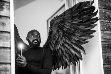 Man in black with dramatic wings holding candle near window