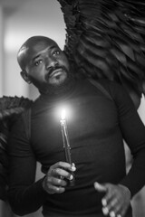 Man with black wings holding a candle in ethereal monochrome setting