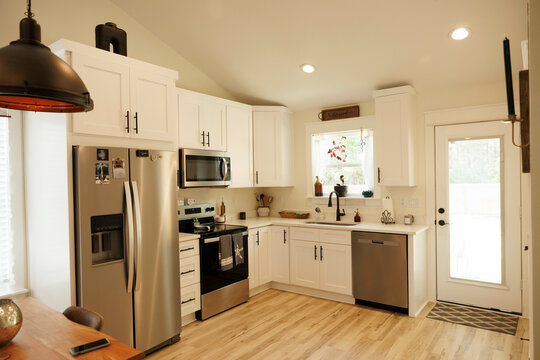 Modern kitchen interior with white cabinets, stainless steel appliances, and hardwood flooring illuminated by natural light, Florida, USA