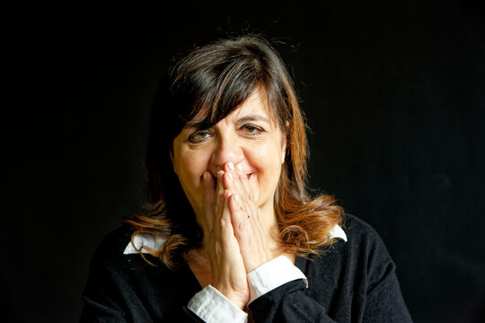 A smiling thankful woman with hands clasped near her face against a dark background.