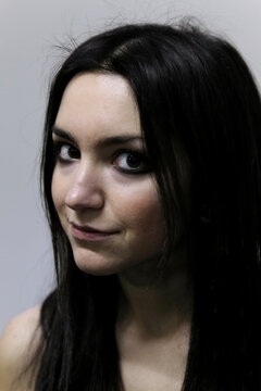 Portrait of a smiling young woman with long dark hair and a subtle gaze against a grey background, Milan, Italy