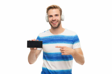 Generation z guy showing phone screen, copy space. Modern phone with headphones isolated on white. Millennial man listening to music in headphones. Man with headphones using phone. Point finger