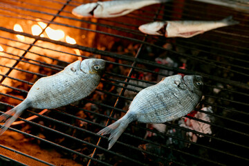 Two fish being grilled on a wire mesh over a flaming grill.