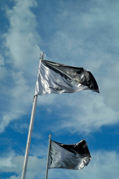 Two black flags flutter against a backdrop of a blue sky with scattered clouds.