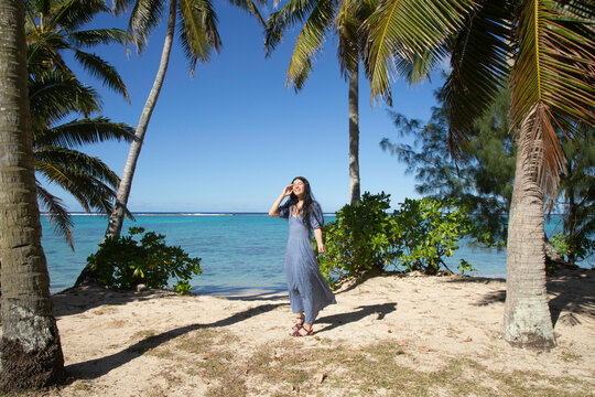 Woman smiling and walking on a tropical beach with palm trees and clear blue sky, Titikaveka, Rarotonga, Cook Islands