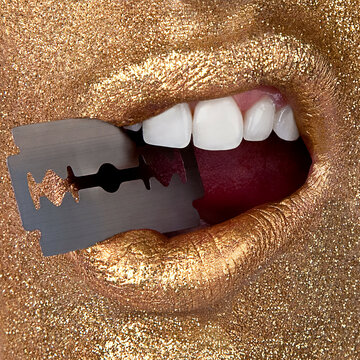 Close-up of a mouth with golden lipstick holding a small blade between the teeth, set against a sparkling gold background.