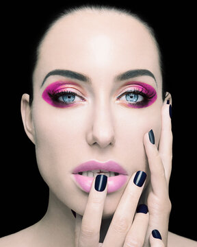 Close-up portrait of a woman with bold pink eyeshadow and lipstick, showcasing her manicured nails against her cheek.