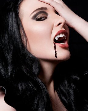 Woman with dramatic makeup and blood dripping from her mouth against a black background.