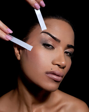 Close-up of a woman removing a facial cleanser strip from her nose against a black background.