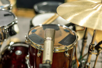 Close-up of a microphone in front of a drum set with a cymbal, showcasing a music recording or performance setup.