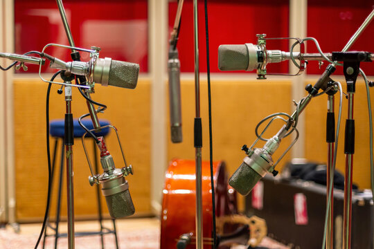 Microphones on stands in a recording studio with a guitar and equipment in the background.