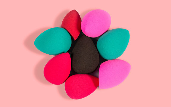 Assorted colorful makeup sponges arranged in a flower pattern on a white background.