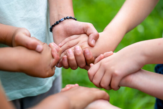 Close-up of children's hands stacked together in a gesture of teamwork and unity on a blurred green background.