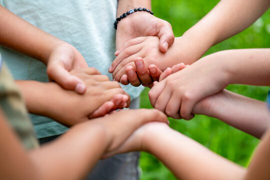 Children's hands stacked together in unity against a green, natural background.