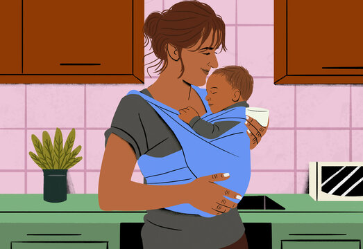 Smiling woman holding a sleeping baby in a blue sling in a cozy kitchen setting.