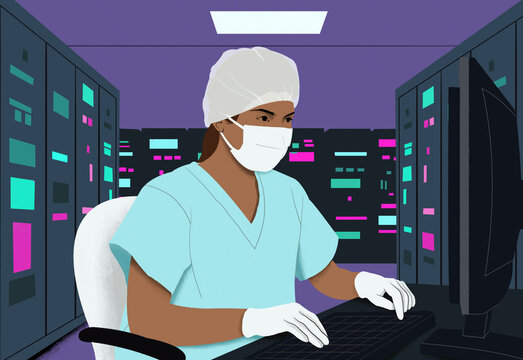 Health professional in scrubs working at a computer in a server room with a protective mask and cap.