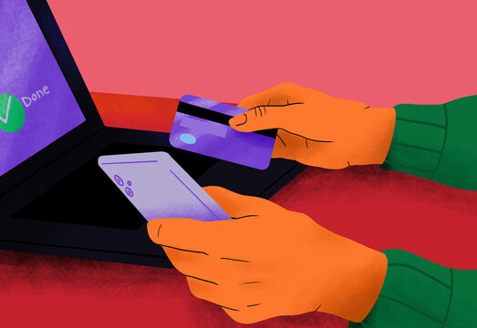 Close-up of hands holding a smartphone and a credit card with a laptop in the background.