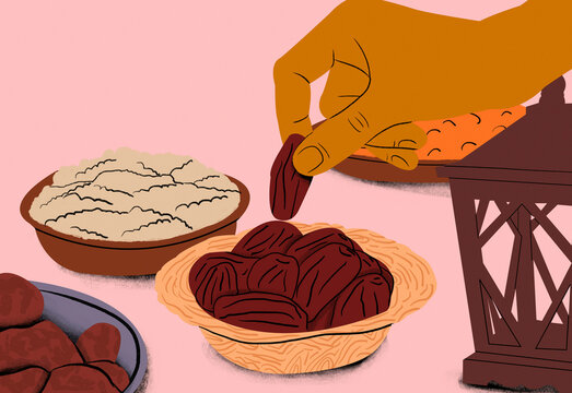Hand picking a date from a bowl with other dry fruits and traditional lantern on a pink background.