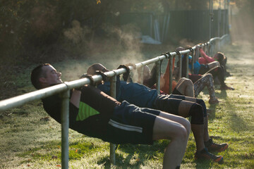 Group of people performing outdoor pull-up exercises on a row of bars on a sunny morning with visible breath in the cool air