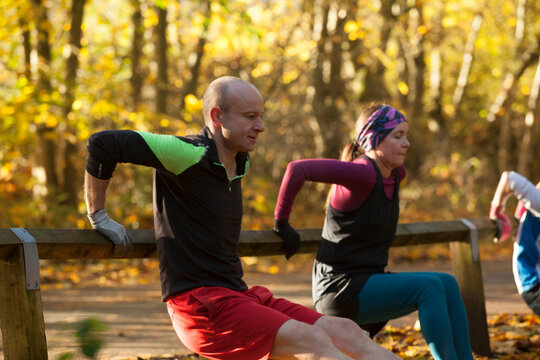 Group of people performing tricep dips on wooden railings in an autumn park setting.