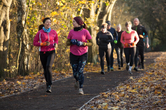 Group of adults jogging together on a leaf-strewn path in an autumn setting.