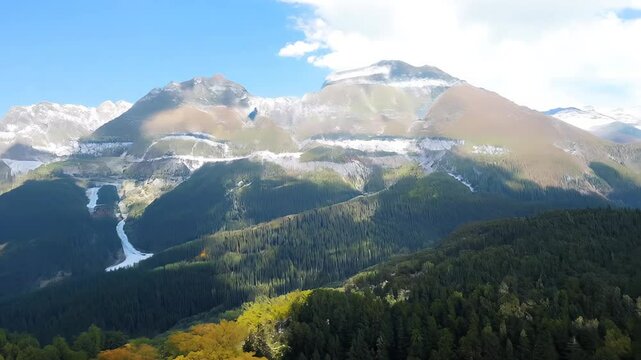 Scenic view of majestic mountains with patches of snow, lush green forests, and a clear blue sky.