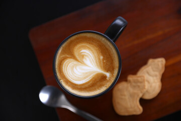 Hot Cappuccino coffee with black cup on old wooden table with isolate in black background