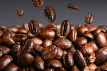 Roasted coffee beans falling on heap against grey background, closeup