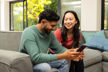 Obraz premium Using smartphone and enjoying conversation together, smiling diverse friends sitting on couch