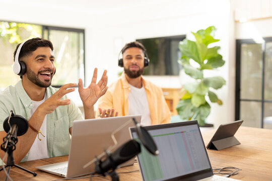 Recording podcast, two friends wearing headphones and using laptops in home studio