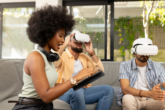 Using VR headsets, diverse friends exploring virtual reality while woman with tablet assists