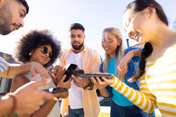 Group of young diverse friends using smartphones and tablets, enjoying outdoor time together