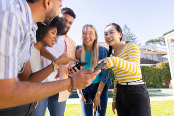 Obraz premium Group of young diverse friends outdoors, laughing and looking at smartphone together