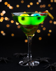 Halloween celebration. Festive green cocktail with eyes, jelly worms and spiders. Close-up. Selective focus.