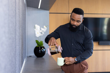 Pouring coffee into mug, african american businessman taking break in modern office kitchen