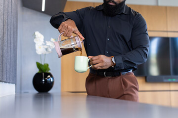 Pouring coffee from French press into mug, man preparing drink in office kitchen