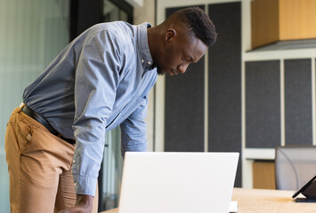 Working in office, man leaning over desk and focusing on laptop screen