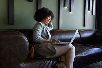 Working on laptop, businesswoman sitting on leather couch in modern office