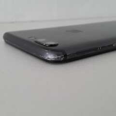 A close-up shot of a black smartphone's corner, highlighting a minor scratch.