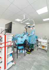 Surgeons in a sterile environment. Two surgeons in protective gear work on a patient in a clean, well-lit surgical room using advanced medical equipment.