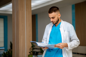 Doc reviewing patient files indoors. A healthcare worker in scrubs studies patient files while...
