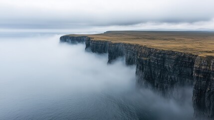 Cliffs covered in mist above calm ocean waters, creating a tranquil and serene atmosphere. The towering rock formations rise from the fog, blending into the quiet landscape.