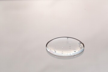 A clear droplet of water rests on a smooth surface, reflecting light.