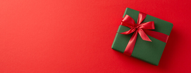 Green gift box wrapped with a red ribbon, placed on a red background, highlighting holiday celebration themes