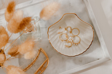Golden jewelry on ceramic tray closeup, feminine dressing table with organizer and sunlight shadows. Luxury golden earrings and rings