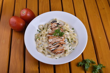 Fettuccine Alfredo with chicken served in a bowl, captured from an angle view. The creamy sauce and pasta create an appealing presentation for a restaurant setting.