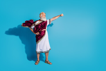 Full body photo of handsome senior male raise fist flying superhero wear ancient greek god king dress isolated on blue color background