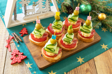 Creative appetizers christmas. Canapes Christmas tree of salami, cheese, olives, tomatoes and cucumbers with baguette on a rustic table.